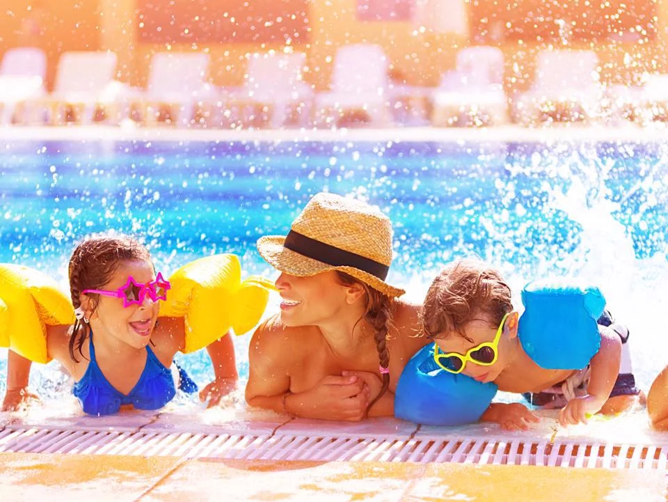 Children relaxing and playing at the edge of a swimming pool during a family pool party
