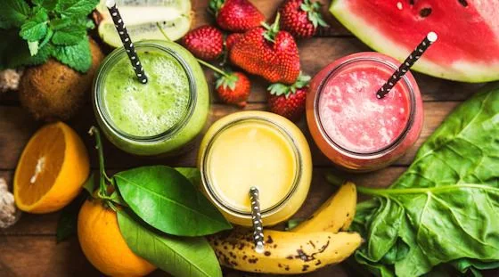 Fresh fruit smoothies surrounded by strawberries, watermelon, citrus, and leafy greens