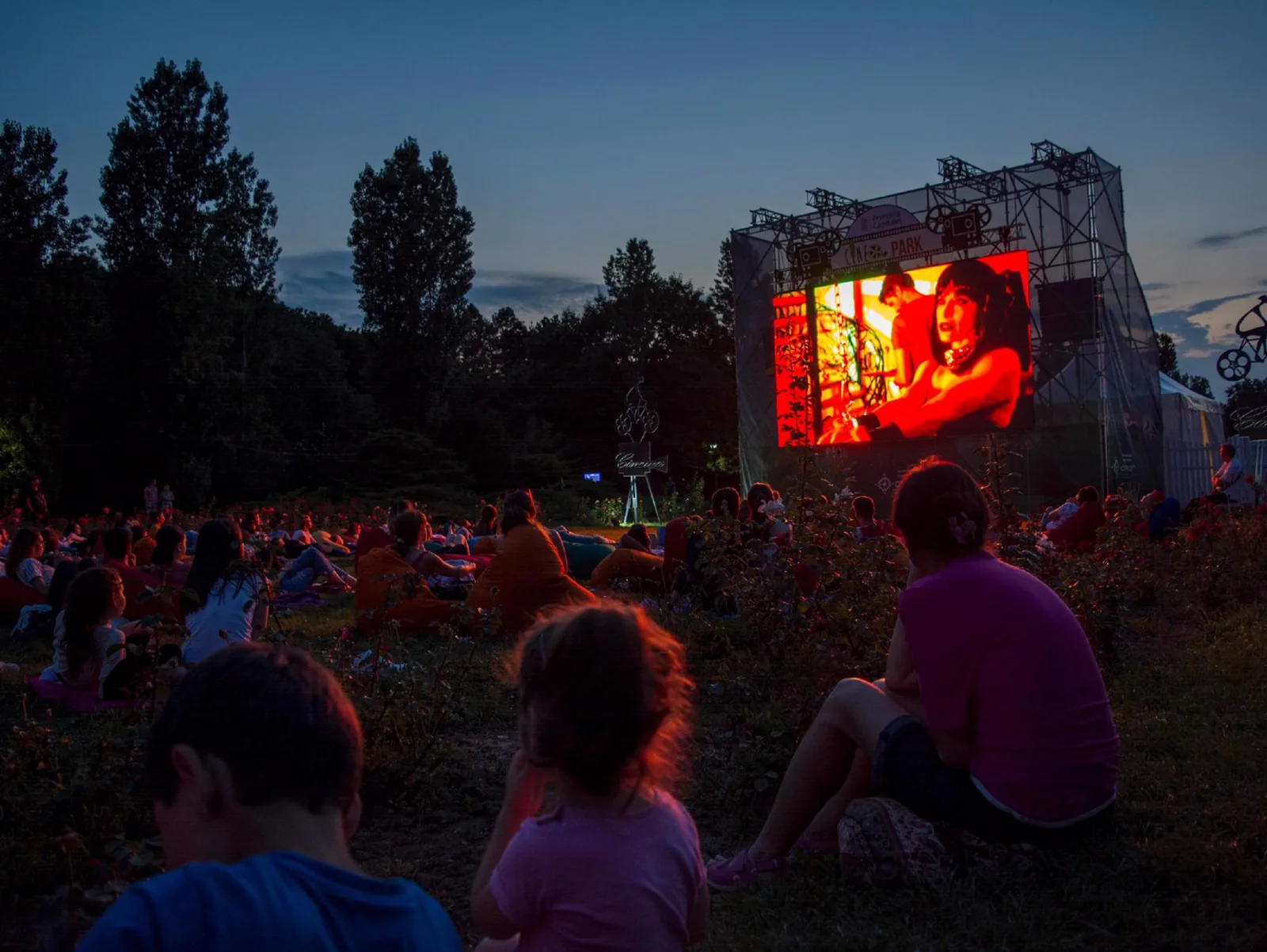 Guests watching a movie on a large outdoor screen during a summer evening event