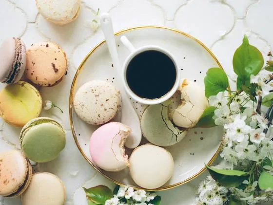 Cup of tea surrounded by colorful pastel macarons and flowers