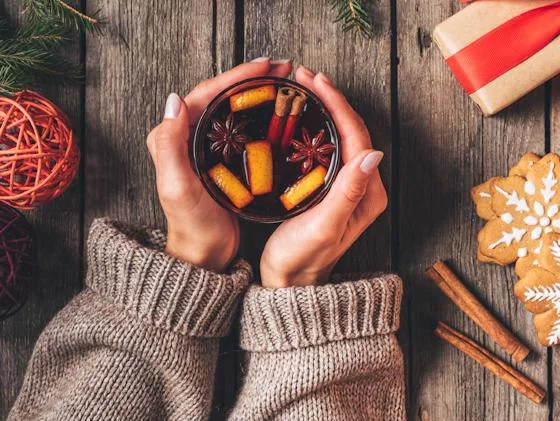 Hands holding a warm mulled wine with cinnamon and holiday spices