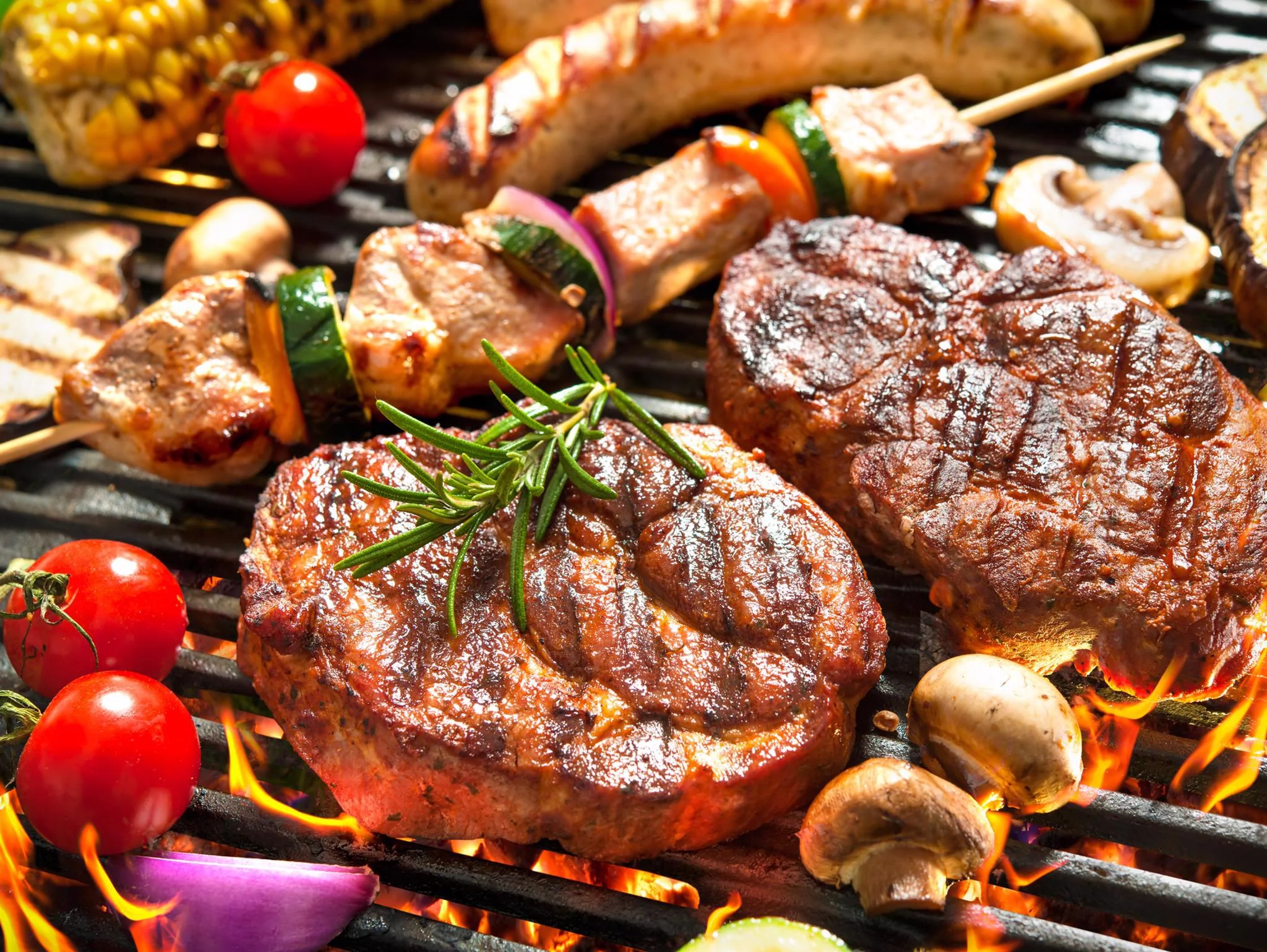 Grilled steak, sausage, vegetables, and corn on an outdoor grill
