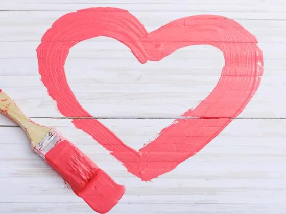 Pink painted heart on a white wooden background with a paintbrush